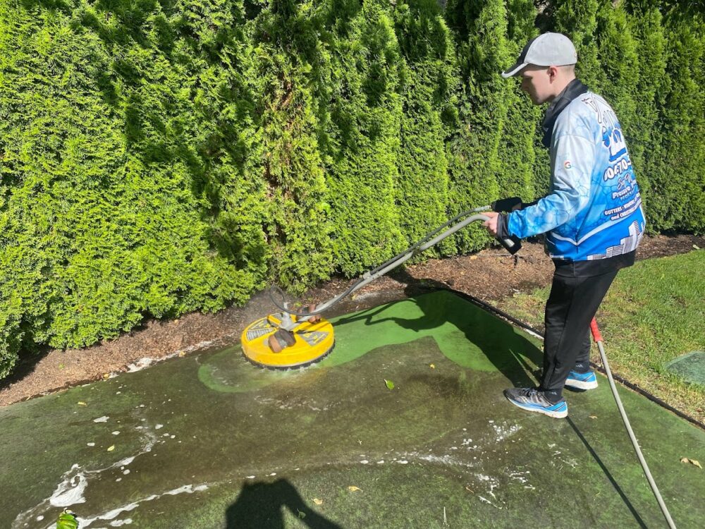Shine City technician using a surface cleaner on an algae-covered concrete driveway in Surrey BC